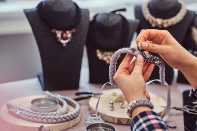 Elegantly dressed woman makes handmade necklaces in jewelry workshop.